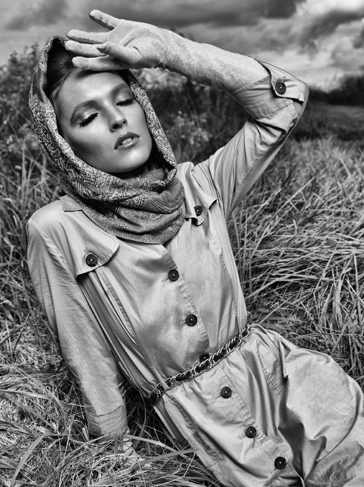 CASTAWAY_Model Megan Wearing Rain Coat Scarf With Arm Raised And Angled Using Gloved Hand To Shield  Face In Field Of Tall Grass Inclining