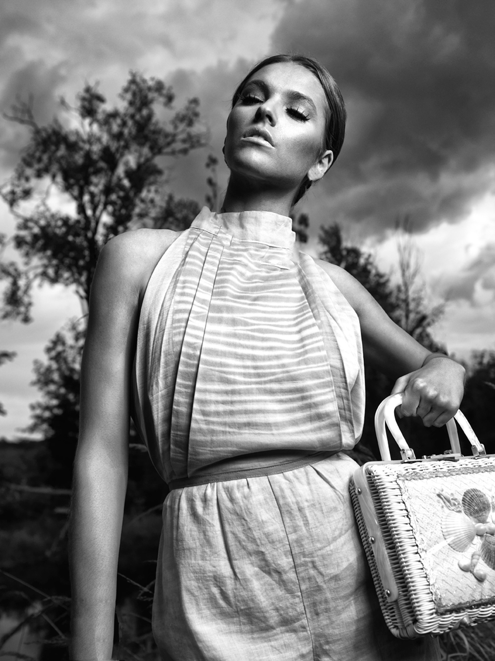 CASTAWAY_Model Megan In Linen Outfit Holding Purse Near Hip Framed Looking Up With Up  With Trees And Sky In Background