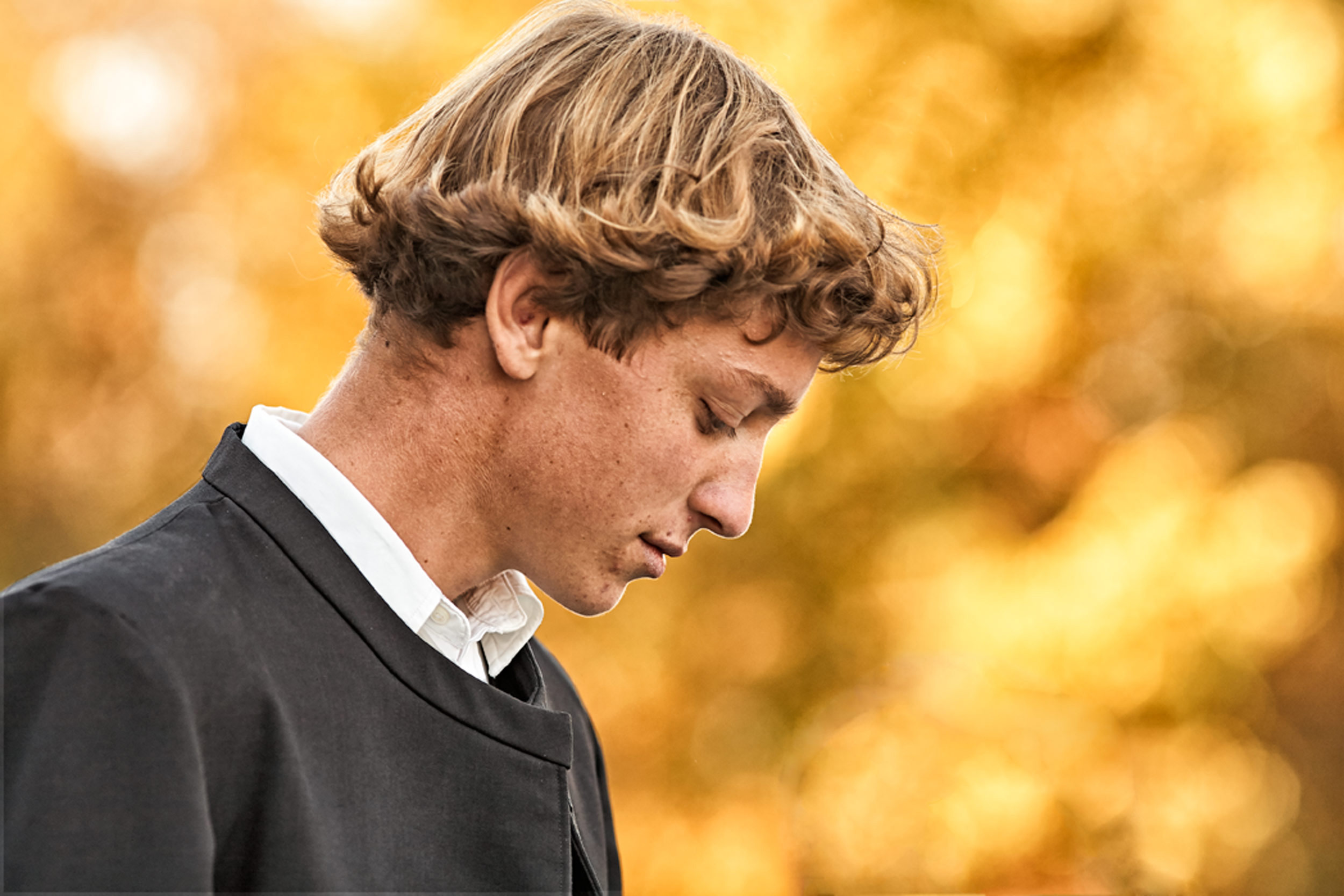 Lifestyle Portrait With West Salem Mission Amish Teen In Black Suit Outside Fall Foliage Using Bokeh To Enhance Scene At Warsaw CMI Revival 