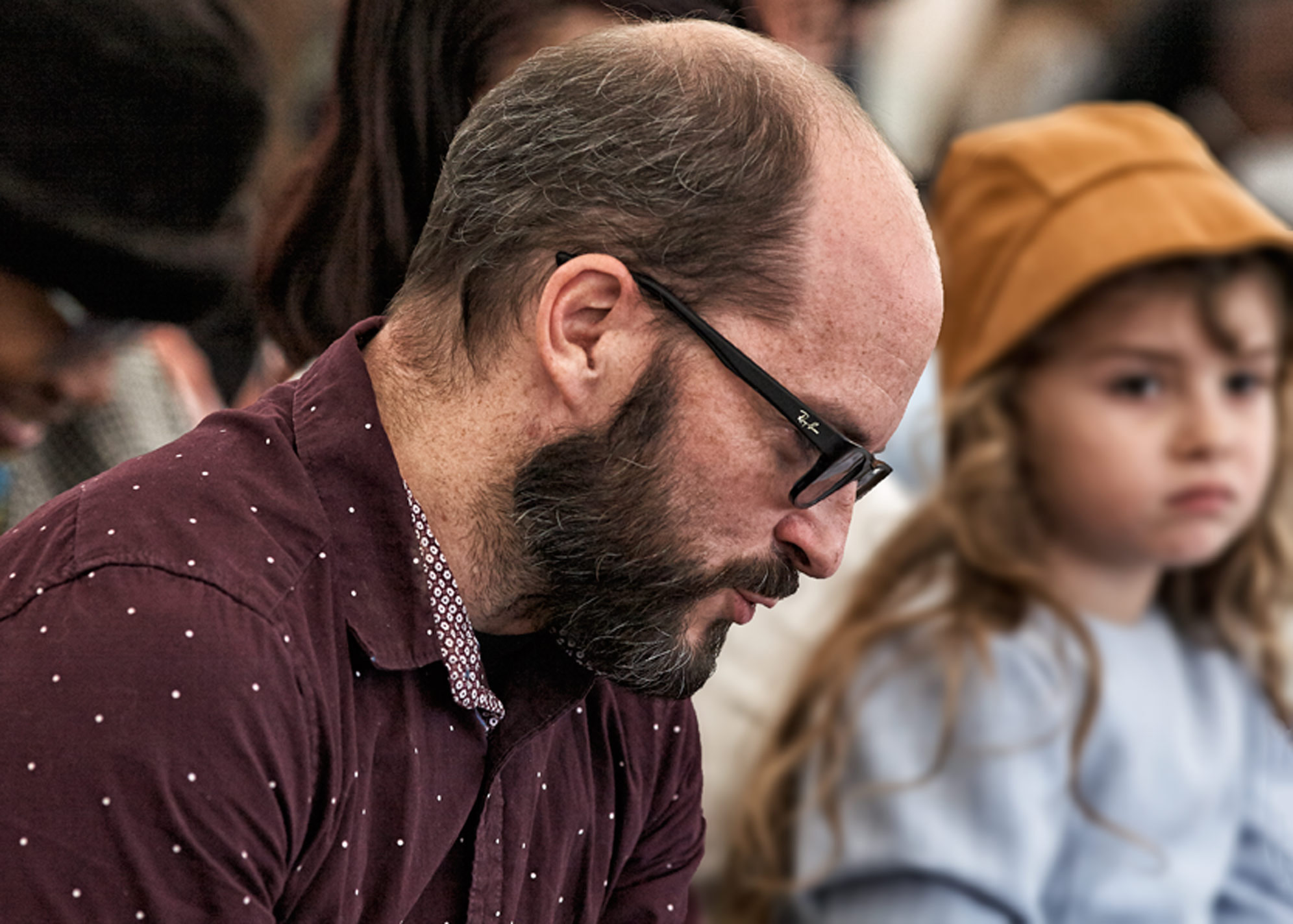  Lifestyle Portrait Of Seated Father In North Central Ohio With Receding Hair Line And Beard Wearing Black Glasses Peering Down Child Adjacent Using Bokeh To Enhance Scene  At Warsaw CMI Revival By An Ohio Commercial Photographer Dennis Harber 