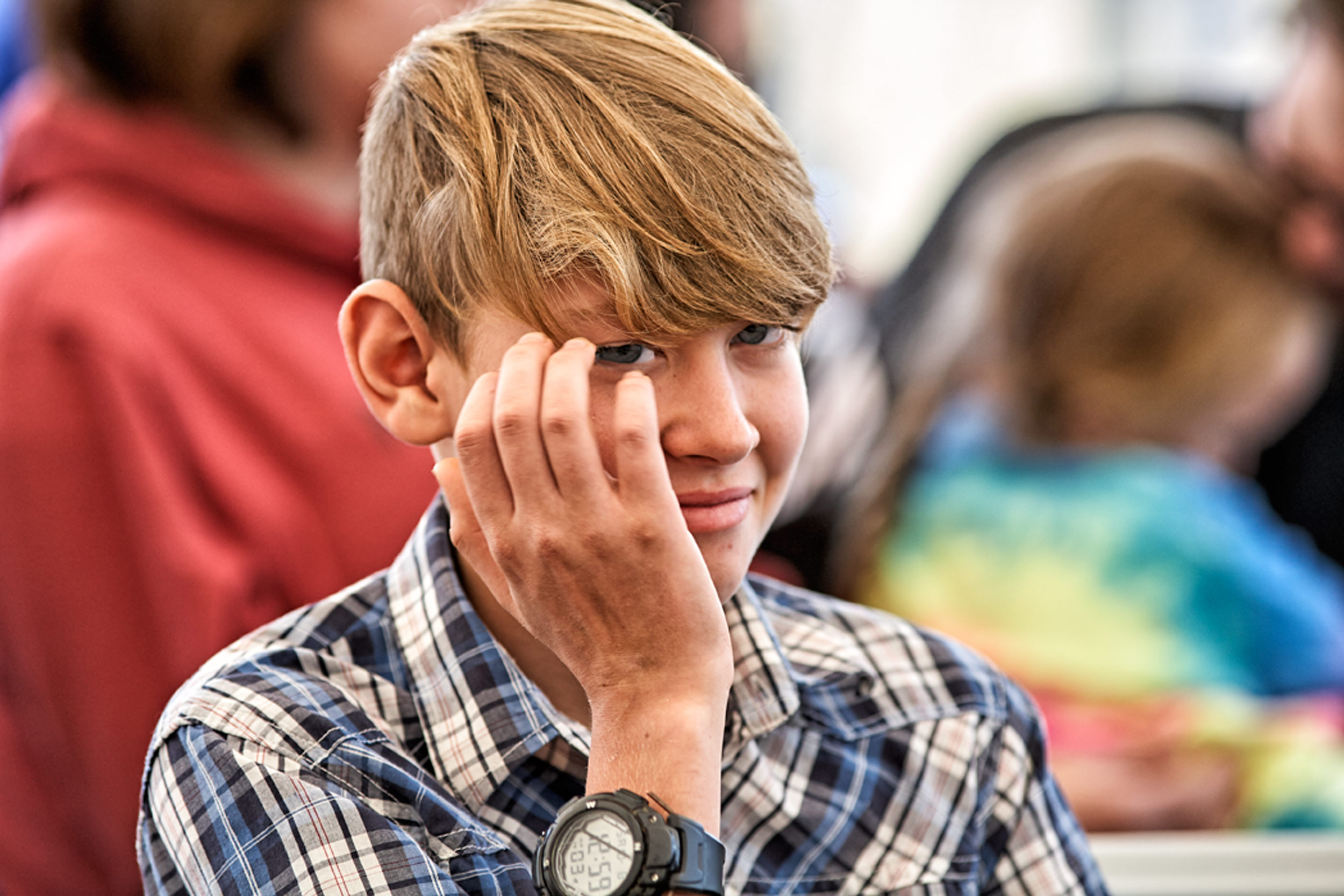 Lifestyle Portrait Photographer With Teenager In Plaid Collared Shirt Black Watch On Hand Over Face Using Bokeh To Enhance Scene At Warsaw CMI Revival By An Ohio Commercial Photographer Dennis Harber
